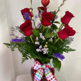 Red roses in a vase with purple filler and a heart pick