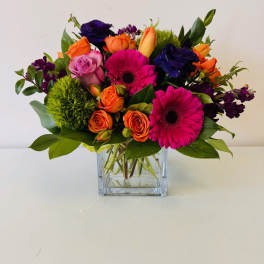 Mixed bouquet of pink gerberas, orange and purple roses in a glass vase