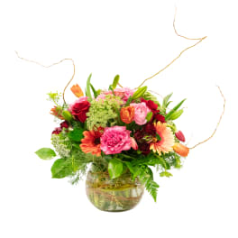 Mixed pink, red, and orange flowers in a round glass vase