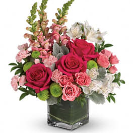 Pink roses and mixed blooms arranged in a square glass vase