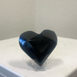 Black faceted heart-shaped decorative object on a clear stand