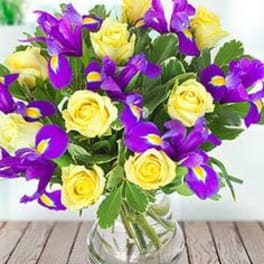 Yellow roses and purple irises in a clear glass vase