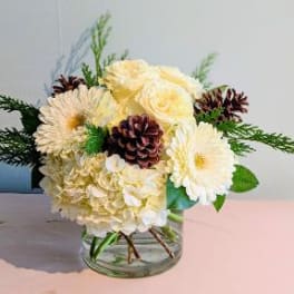 Cream floral arrangement in a clear glass vase with pinecones and greenery