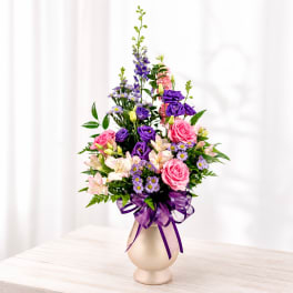 Pink and purple mixed bouquet in a beige vase with a purple ribbon