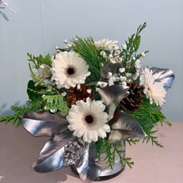 White gerbera daisies in a silver vase with pinecones and metallic leaves