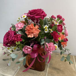 Mixed bouquet of pink and coral flowers in an amber vase with ribbon