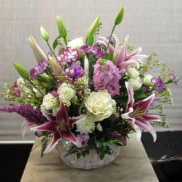 Mixed bouquet of lilies, roses, and purple flowers in a white vase
