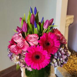 Pink roses and gerbera daisies in a glass vase with purple tulips