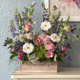 Mixed pink, white, and purple flowers arranged in a wooden box