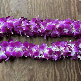 Two purple orchid leis on a wooden surface