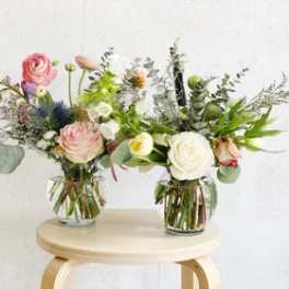 Two mixed flower arrangements in clear glass vases on a stool