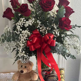 Red roses in a vase with baby’s breath, a teddy bear, and chocolates