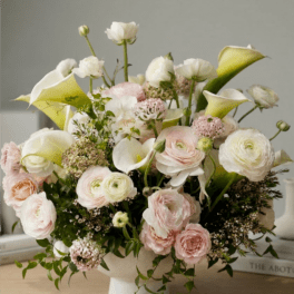 Low arrangement of white calla lilies and pale pink blooms in a white footed bowl