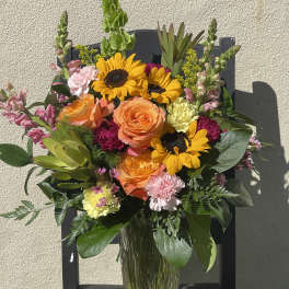 Tall mixed bouquet with sunflowers, orange roses, and pink flowers in a clear glass vase
