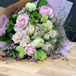 Bouquet of pale pink and cream roses with green blooms wrapped in lavender paper