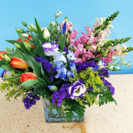 Mixed bouquet in a clear glass vase with pink, purple, blue, and orange flowers