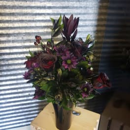 Dark purple bouquet in a black vase with roses and daisy-like blooms