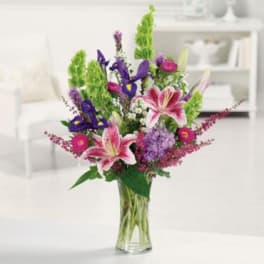 Tall mixed bouquet with pink lilies, purple irises, and green spikes in a glass vase