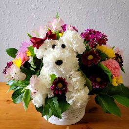 White flower dog arrangement in a white basket with pink and yellow blooms