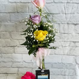Tall bouquet of pink, lavender, and yellow roses with baby's breath and a ribbon