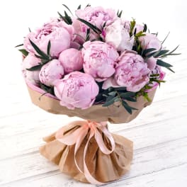 Bouquet of pale pink peonies wrapped in brown paper with a pink ribbon