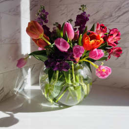 Bright mixed bouquet of tulips and alstroemeria in a round glass vase