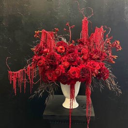 Red floral arrangement in a white pedestal vase