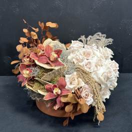 Arrangement of cream roses and burgundy orchids in a low container