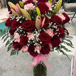 Bouquet of red roses, pink carnations, and lilies in a glass vase