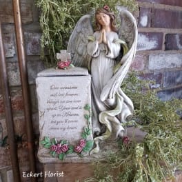Angel memorial statue beside a stone urn with pink roses