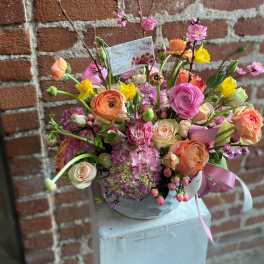 Mixed bouquet of pink, peach, and yellow flowers in a round container
