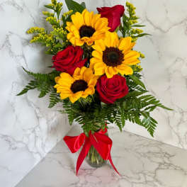 Bouquet of red roses and yellow sunflowers in a glass vase with a red ribbon