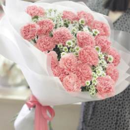 Pink carnations and small white daisies wrapped in white paper with a pink ribbon
