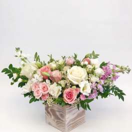 Low floral arrangement of pink, white, and lavender roses in a square vase