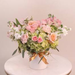 Pink and peach roses arranged with white blooms in a white vase