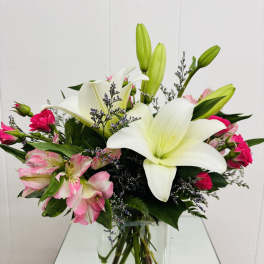 White lilies and pink flowers arranged in a clear glass vase