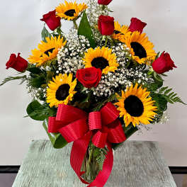 Bouquet of red roses and sunflowers with a red ribbon in a glass vase