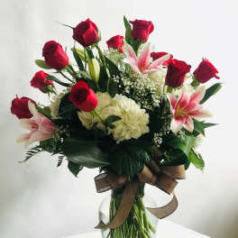 Red roses and pink lilies in a glass vase with a brown ribbon