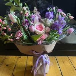 Bouquet of pink and purple flowers wrapped in paper with a lavender ribbon