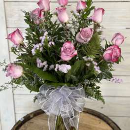 Pink roses arranged in a clear glass vase with a white ribbon bow