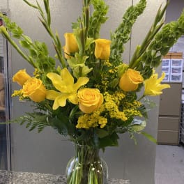 Yellow roses and lilies in a clear glass vase with tall green spikes