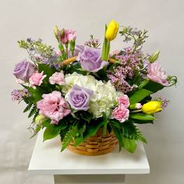 Basket arrangement with lavender roses, pink carnations, white hydrangea, and yellow tulips