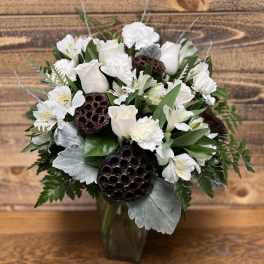 White floral arrangement in a glass vase with lotus pods and silver foliage