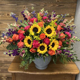 Mixed bouquet with sunflowers, orange roses, and purple flowers in a gray vase