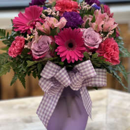 Pink and purple mixed bouquet in a lavender vase with a plaid ribbon