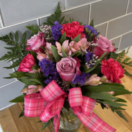 Bouquet of pink and purple flowers in a glass vase with a pink plaid ribbon