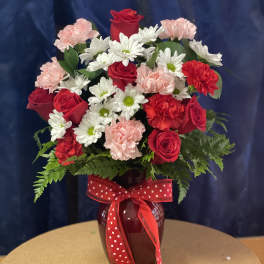Red roses, white daisies, and pink carnations in a vase with a red polka-dot ribbon.