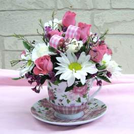 Pink and white flower arrangement in a floral teacup and saucer