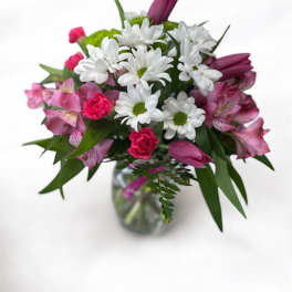 Bouquet of white daisies, pink alstroemeria, and purple tulips in a glass vase