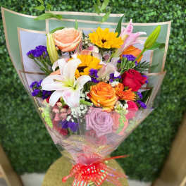 Colorful wrapped bouquet with lilies, roses, sunflowers, and mixed blooms tied with a red ribbon
